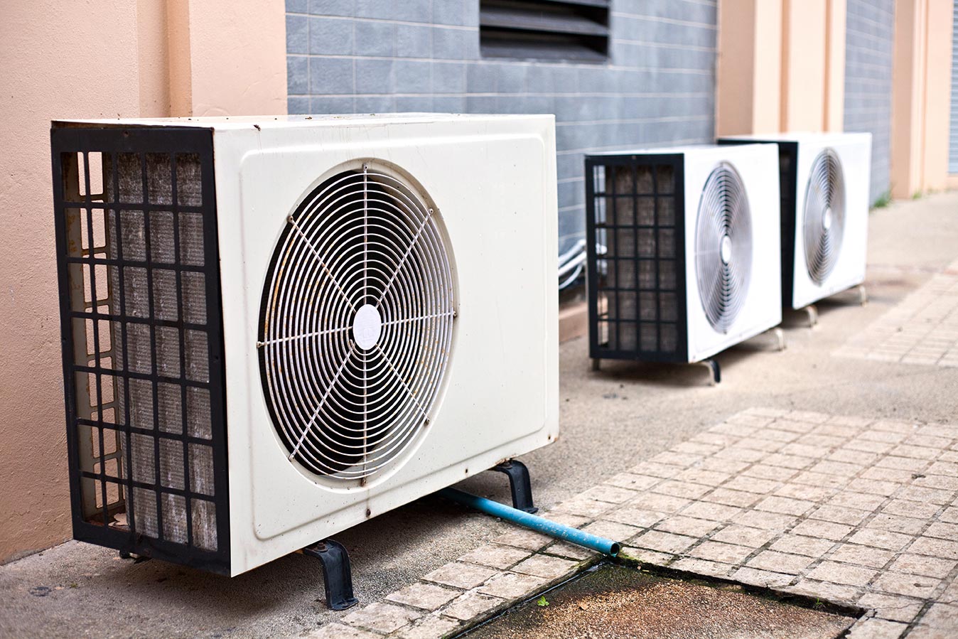 Three air conditioning fans next to a blue and peach colored wall